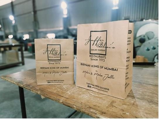 Two sizes of kraft SOS bags printed in one colour with a restaurant's logo and contact details, photographed on the factory floor