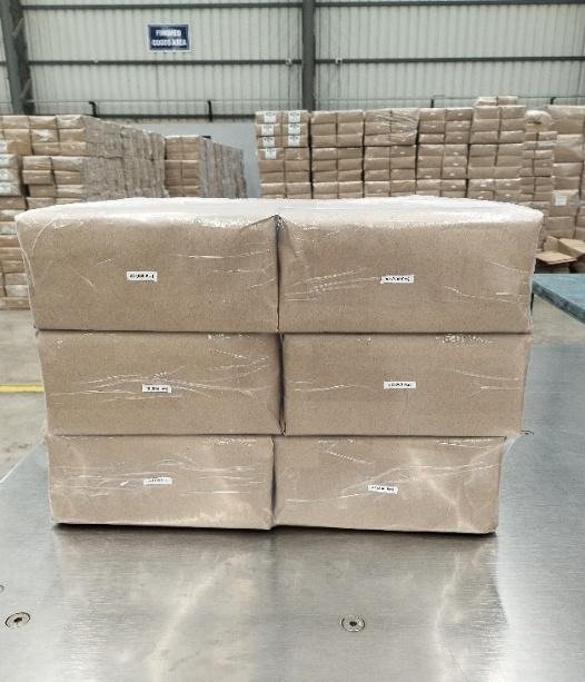 Six kraft-wrapped bales of paper bags stacked and labelled in the finished goods area