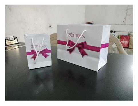 Two white laminated premium paper bags with ribbon handles and printed branding